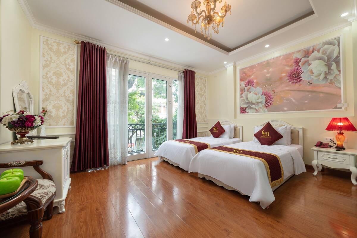A hotel room with two beds, a chandelier, a painting, and a view through the glass doors.