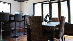 A modern dining area with wicker chairs, a dark wooden table, and bar stools. - Nangoku Lodge Booya (Onna)