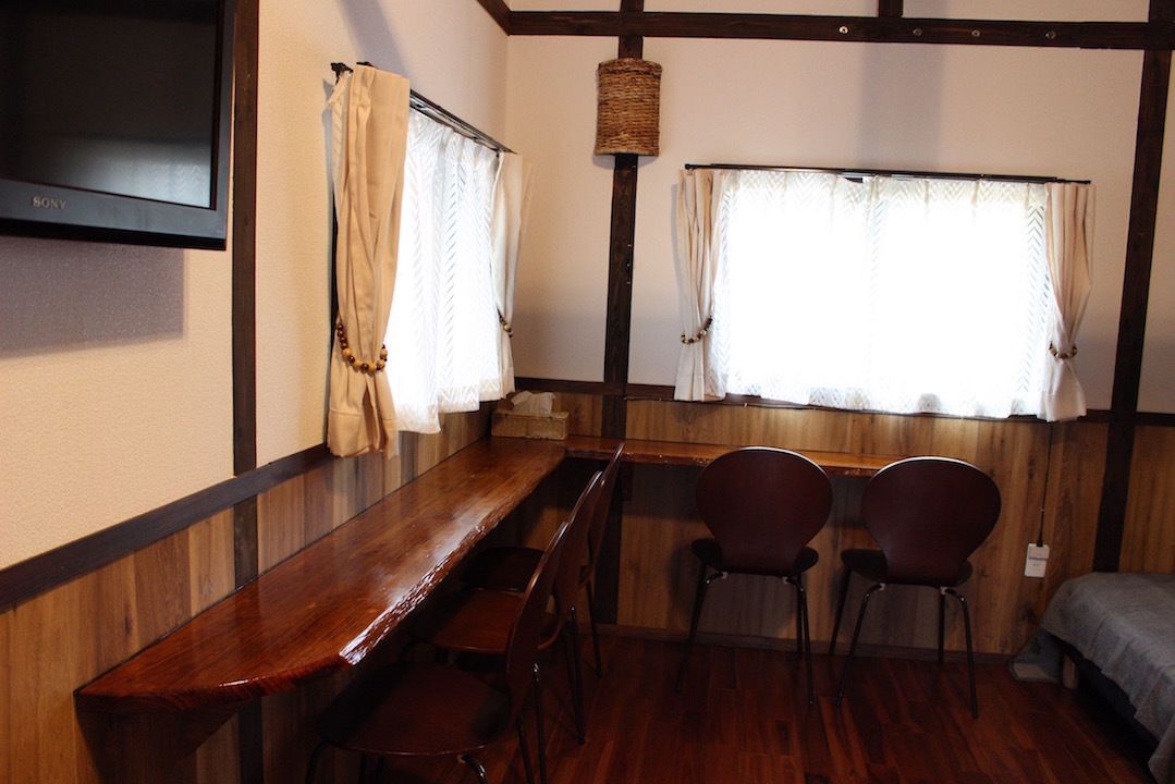 A room with a wooden bench, two chairs, a television, and windows with curtains.