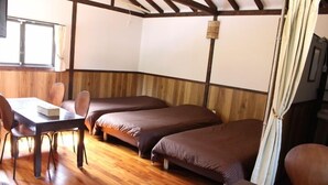 A room with wooden flooring, two single beds, a table with chairs, and a window with curtains. - Nangoku Lodge Booya (Onna)