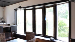 A room with a large window, a table, two chairs, a lamp, and a small shelf with a bowl. - Nangoku Lodge Booya (Onna)