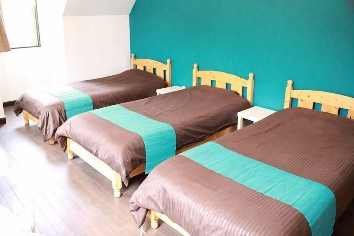 A room with three wooden beds, each with a headboard and footboard, and a small white nightstand between the beds.