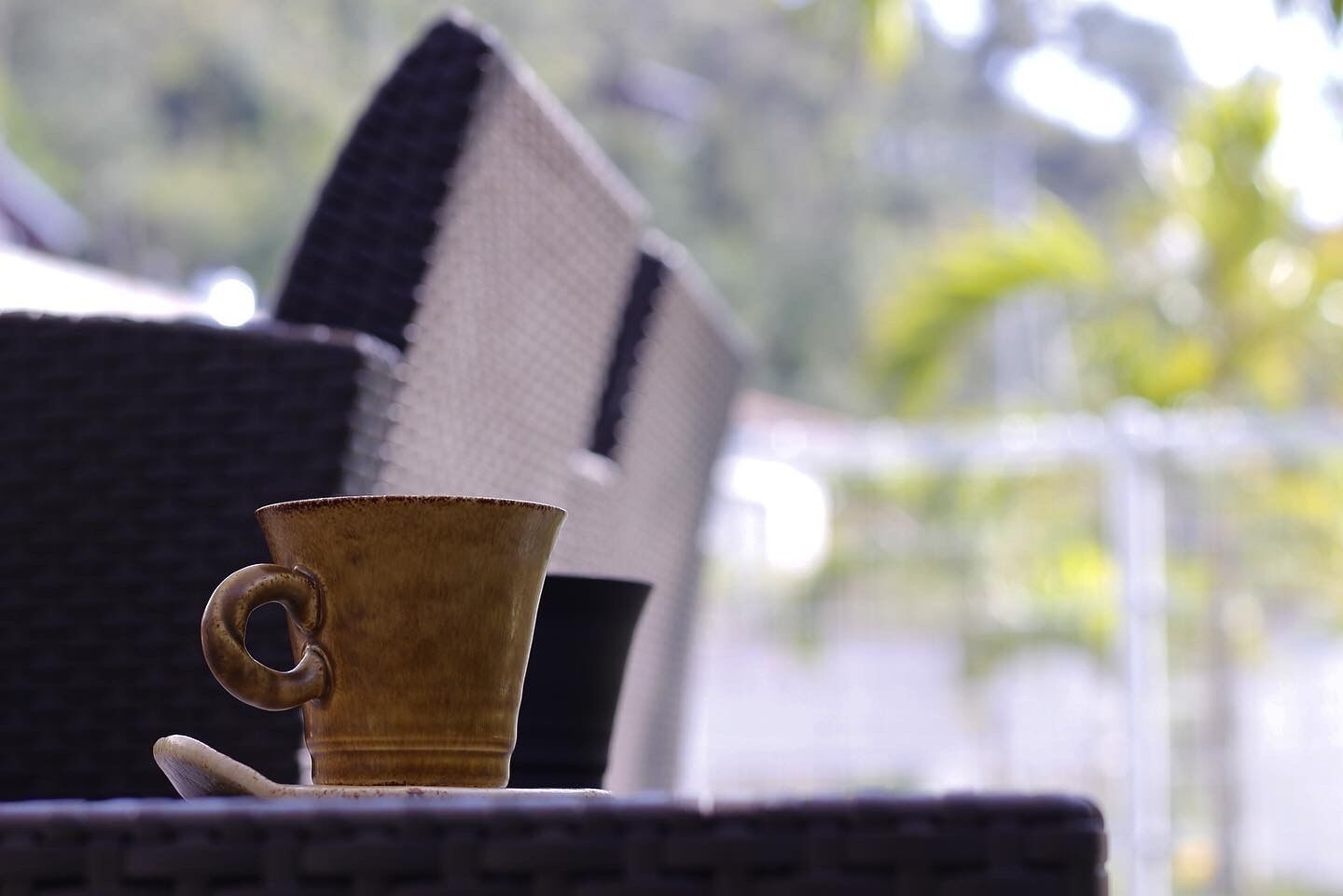 A rustic, textured woven chair with a black and white striped cushion, a small, rustic cup, and a spoon on a wicker table.