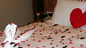 A neatly made bed with rose petals scattered across the bedspread, a heart-shaped pillow, and a folded towel on the side. - Tehran Boutique Hotel (Dogubayazit)