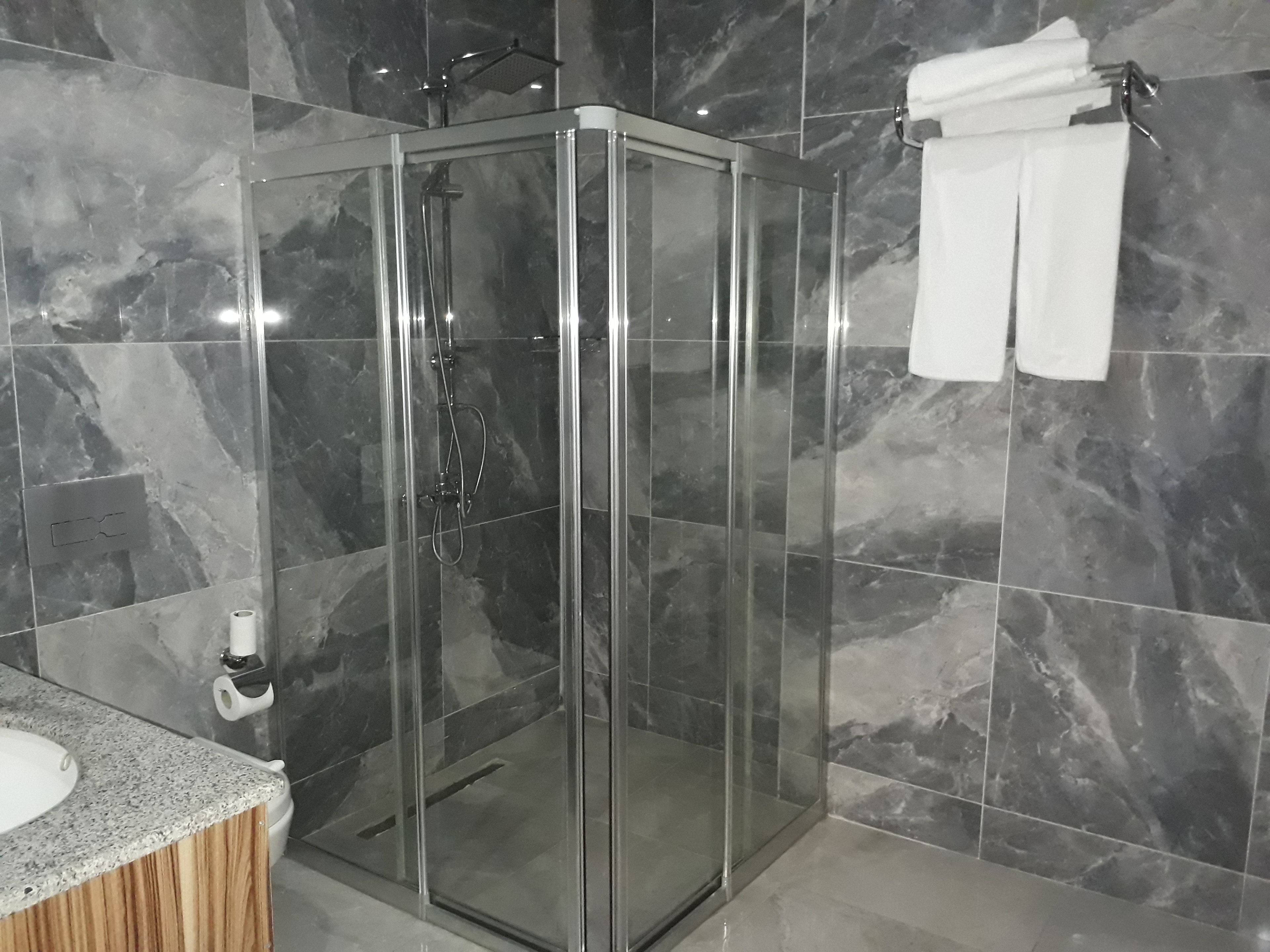 Een moderne badkamer met een douche in glazen cabine, marmeren tegels en een houten wastafelmeubel.