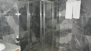 Een moderne badkamer met een douche in glazen cabine, marmeren tegels en een houten wastafelmeubel.
