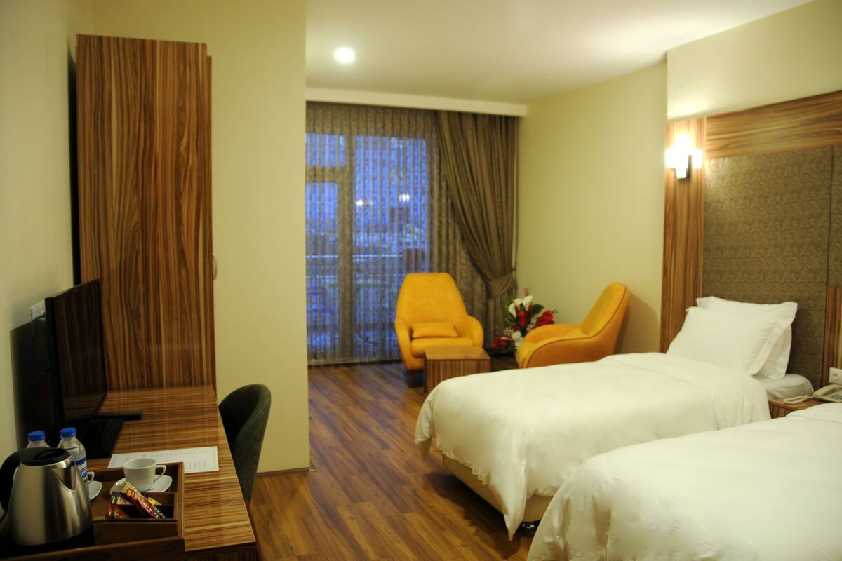 A hotel room with two beds, a desk with a coffee maker, a chair, and a window with curtains.