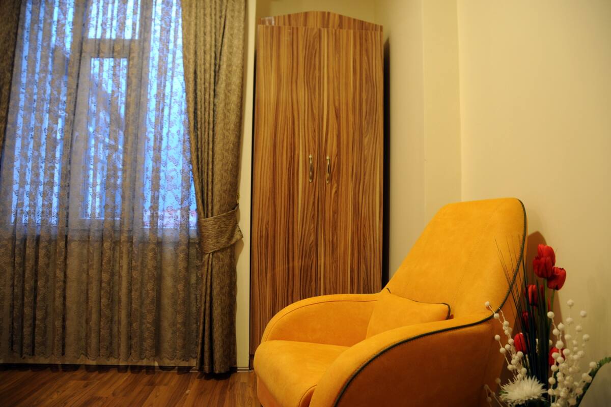 A room with a wooden wardrobe, a yellow armchair, and a window with curtains.