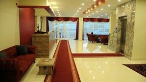 A hotel lobby with a red carpet, a reception desk, a sofa, and a dining area with chairs. - Tehran Boutique Hotel (Dogubayazit)