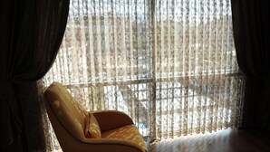 A room with a large window covered by sheer curtains, a wooden floor, and a single yellow armchair. - Tehran Boutique Hotel (Dogubayazit)