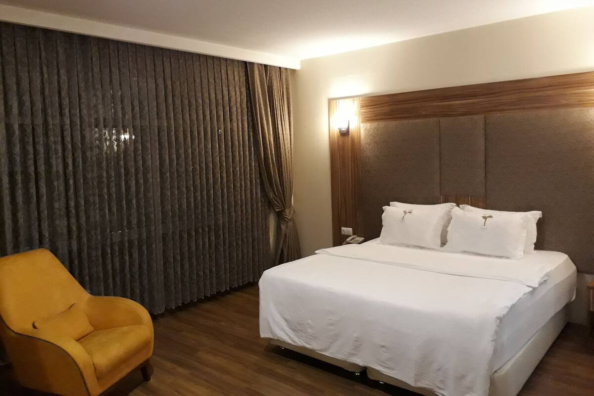 A hotel room with a bed, a chair, a nightstand, and a curtain.