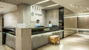 Een moderne receptie met een receptiebalie, een receptionist en een wandbordje met de tekst 'SHANGRIA'.