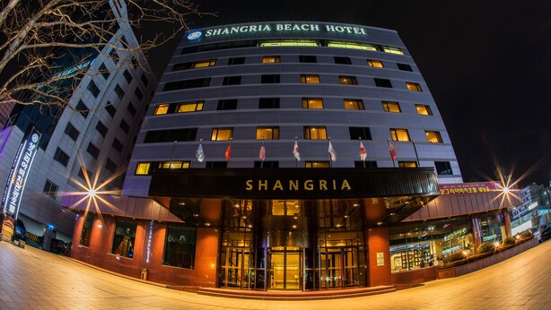Het uiterlijk van het Shangria Beach Hotel, met verlichte borden en de ingang.