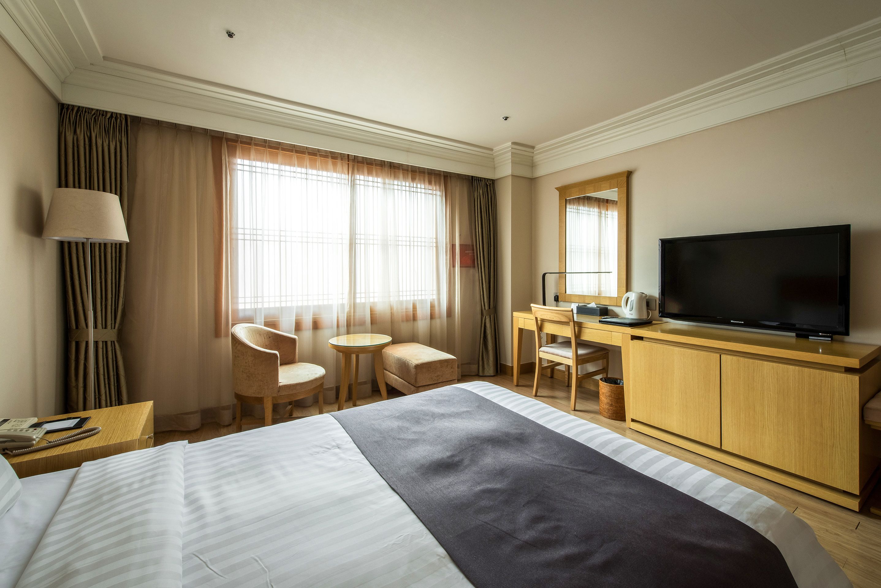 A hotel room with a large bed, a desk with a television, two chairs, and a small table.