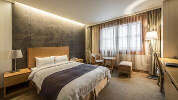 Ein Hotelzimmer mit einem großen Bett, Nachttischen, einem Schreibtisch, einem Sessel und einem kleinen Tisch.