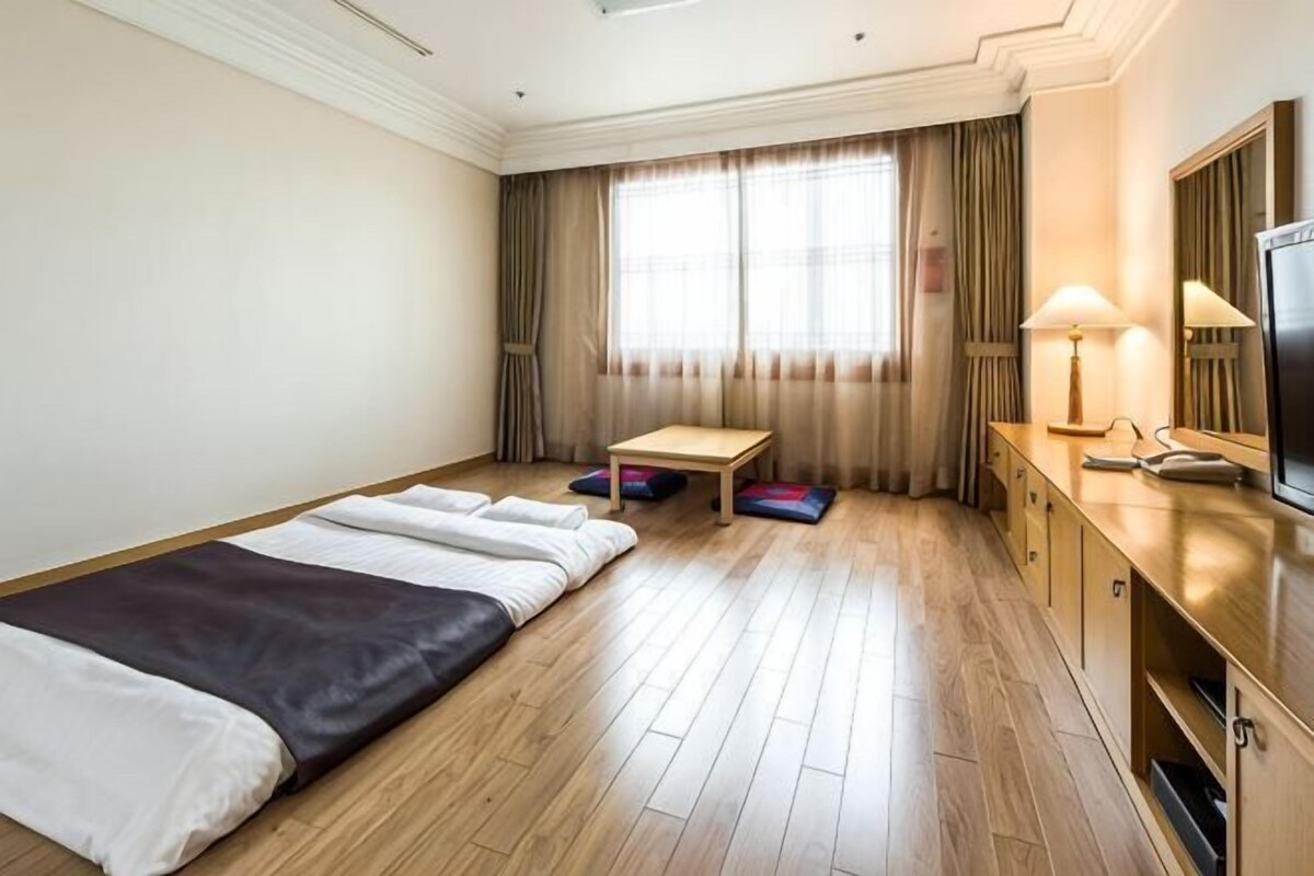 Habitación de hotel con cama, escritorio, silla, televisión y ventana con cortinas.
