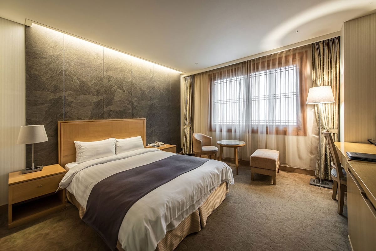 A hotel room with a large bed, bedside tables, a desk, a chair, and a small table.