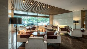 Een moderne lounge met verschillende zitplaatsen, een groot raam met uitzicht op de omgeving en een plafond met houten lambrisering.