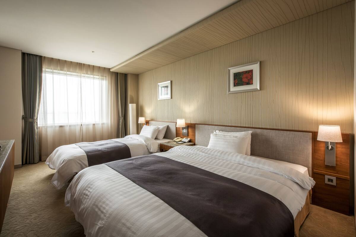 A hotel room with two beds, a desk, and a window with curtains.