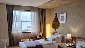 Een hotelkamer met twee bedden, een bureau, een stoel, een raam met gordijnen, een nachtkastje met een lamp en een aan de muur hangend schilderij.