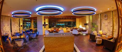 A spacious lobby with a central seating area, multiple tables, and a large stone feature.
