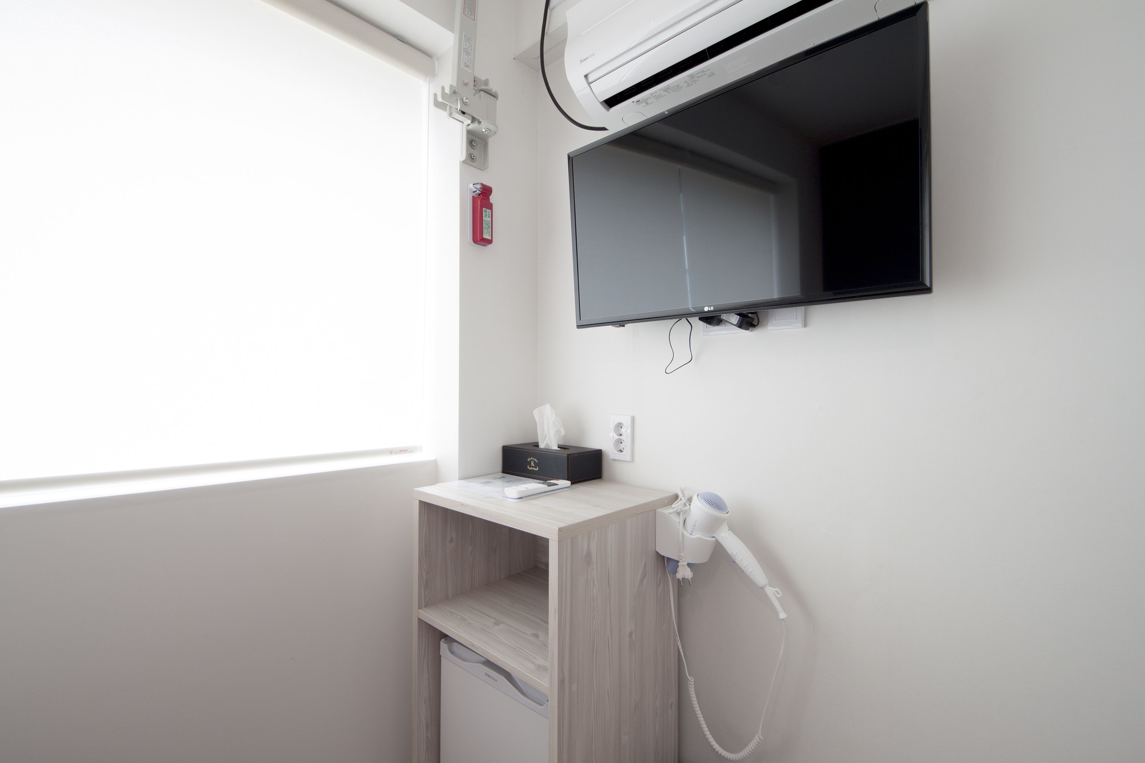 A bathroom with a mounted TV, a hairdryer, and a small shelf with a tissue box.