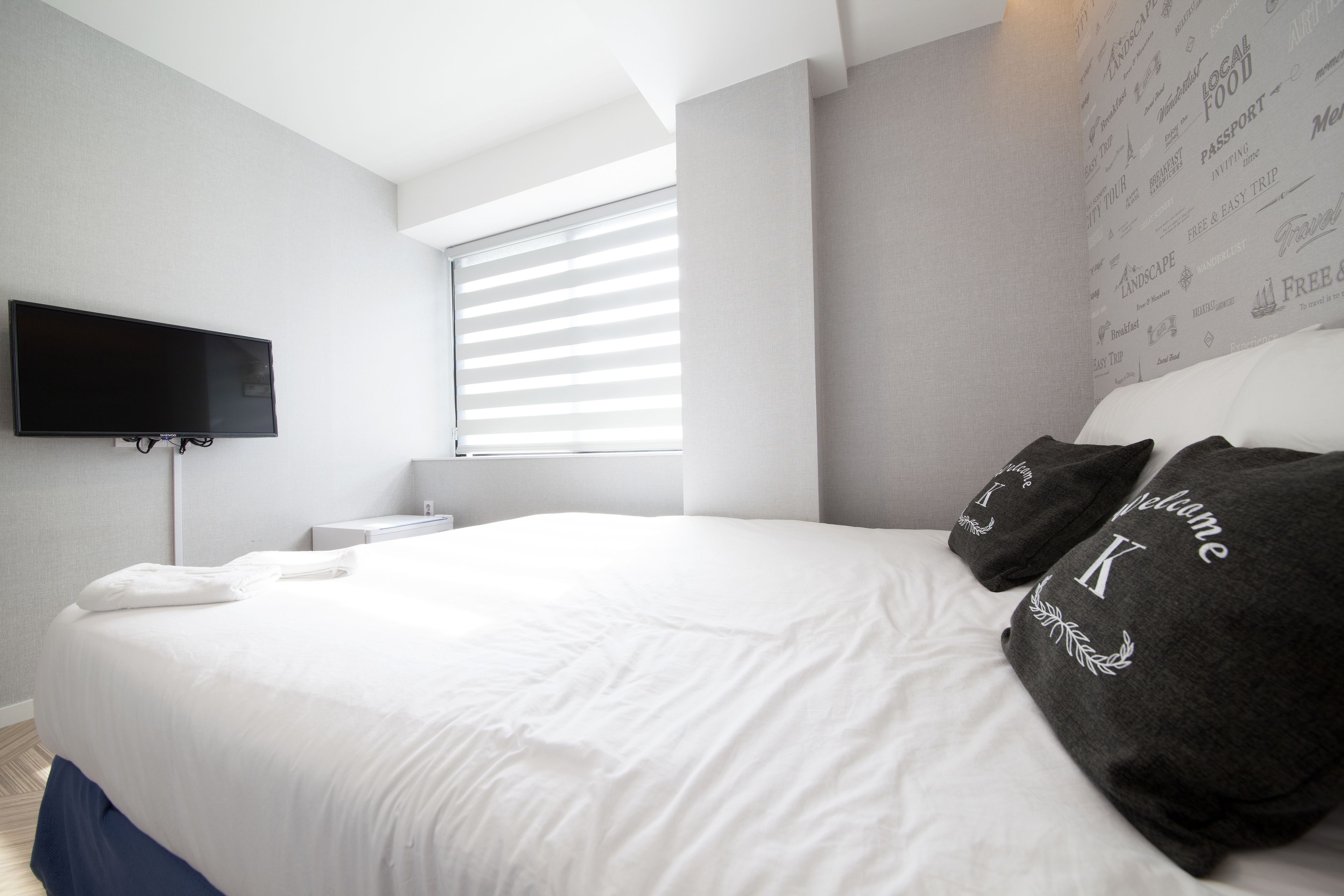 Een moderne hotelkamer met een groot bed, een flatscreen televisie aan de muur en een raam met zonwering.