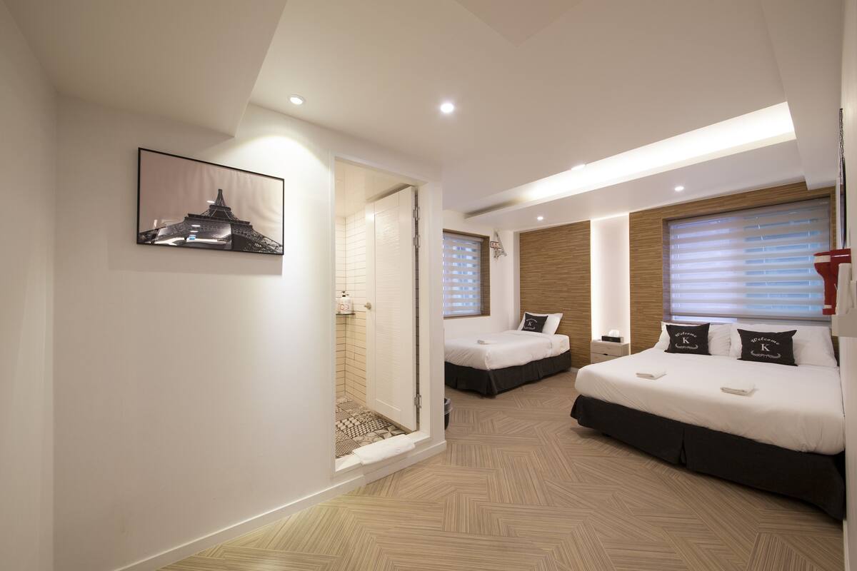 A modern hotel room with a large bed, a smaller bed, a shower area, and a framed picture on the wall.