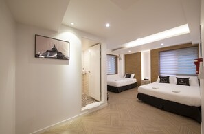 A modern hotel room with a large bed, a smaller bed, a shower area, and a framed picture on the wall.