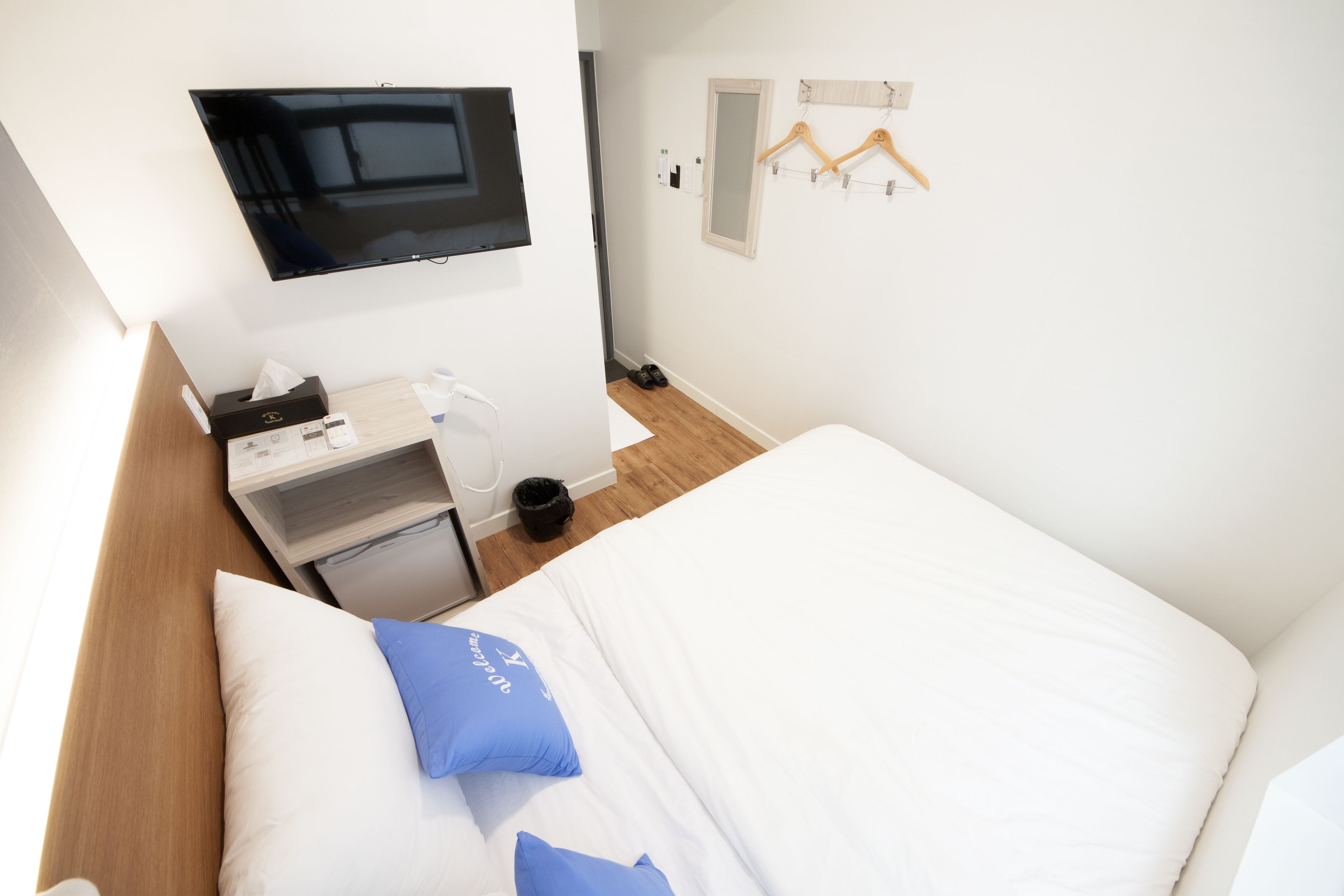 Ein Hotelzimmer mit einem Bett, einem Schreibtisch mit Fernseher, einem Spiegel und einem Kleiderhaken.