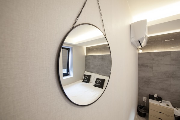 A modern bedroom with a large mirror, a bed with black pillows, a small window, and a wall-mounted air conditioner.