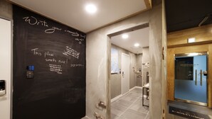 A hallway with a blackboard displaying messages, a reception area with a wooden door, and a tiled floor.