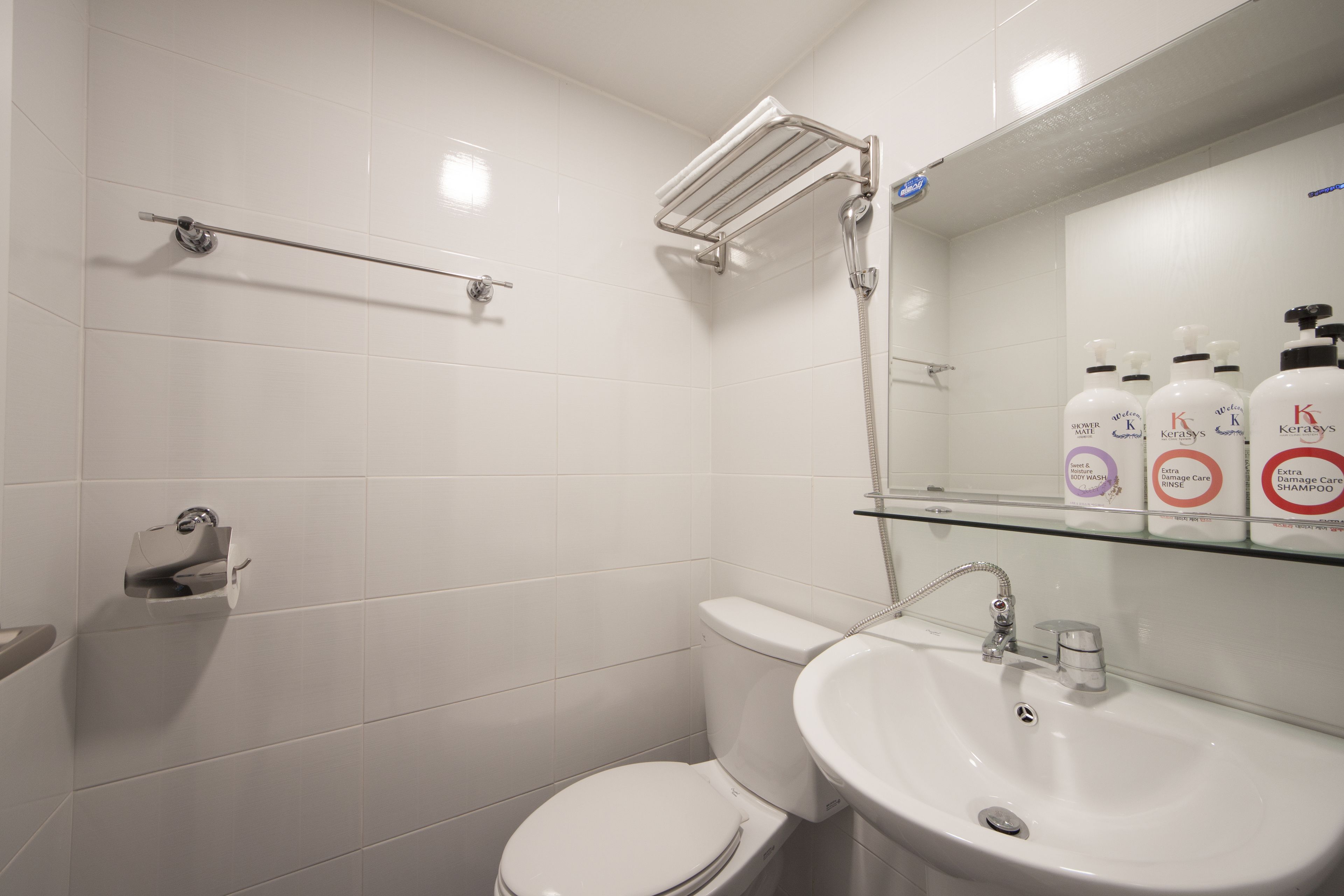 A modern bathroom with a toilet, sink, and shower. There are toiletries on a shelf.
