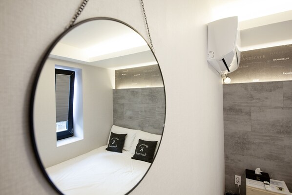 A modern bedroom with a bed, a round mirror, and a window.
