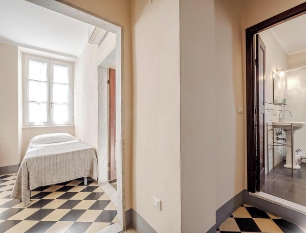 Una habitación con cama, ventana y baño visible a través de una puerta abierta.