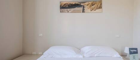 A bedroom with a bed, a nightstand, a lamp, and a wall-mounted picture of a beach.