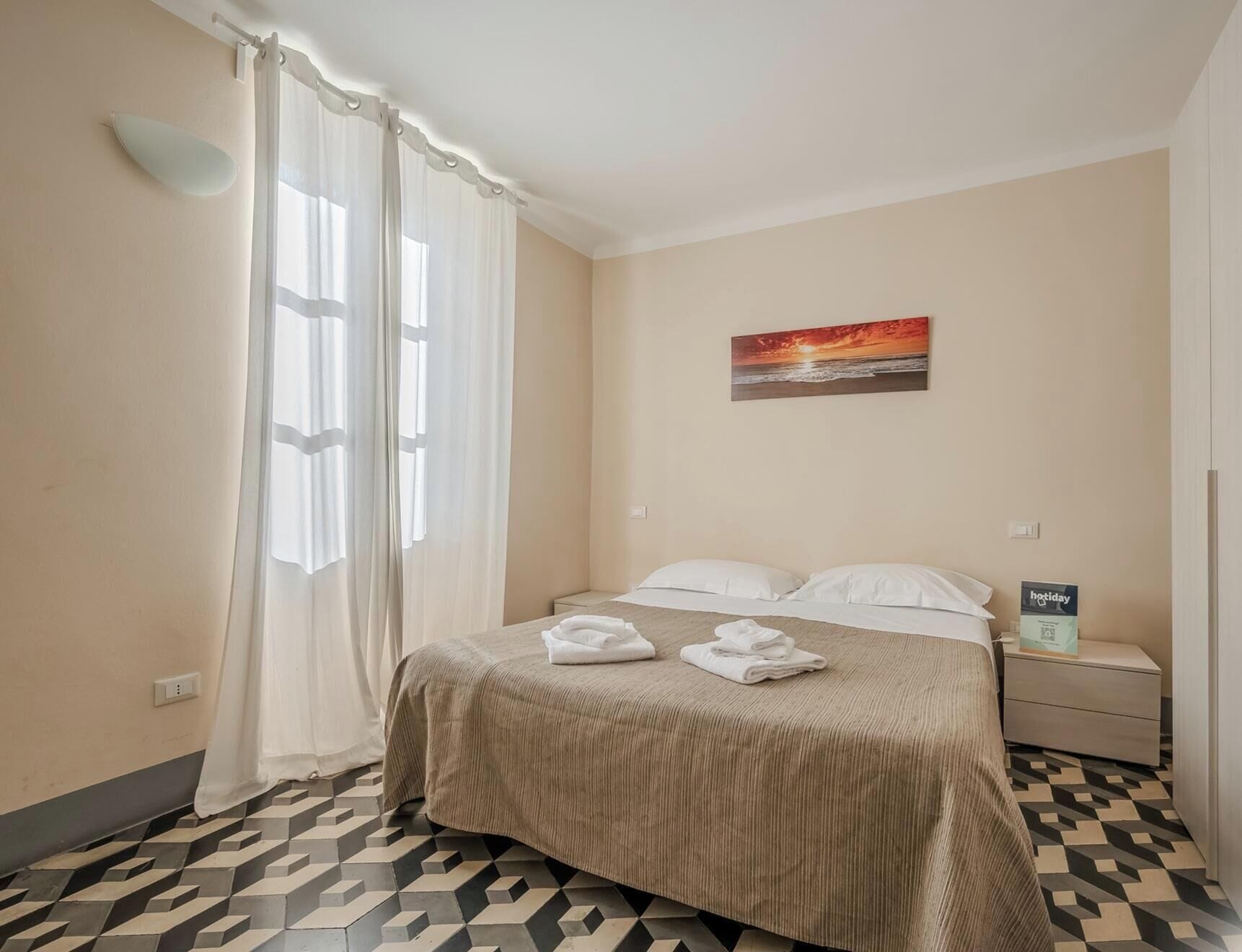 A hotel room with a bed, a nightstand, a painting, and a geometric patterned floor.