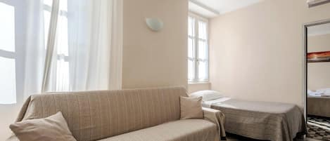 A room with a sofa, a bed, a checkered floor, and a window with curtains.