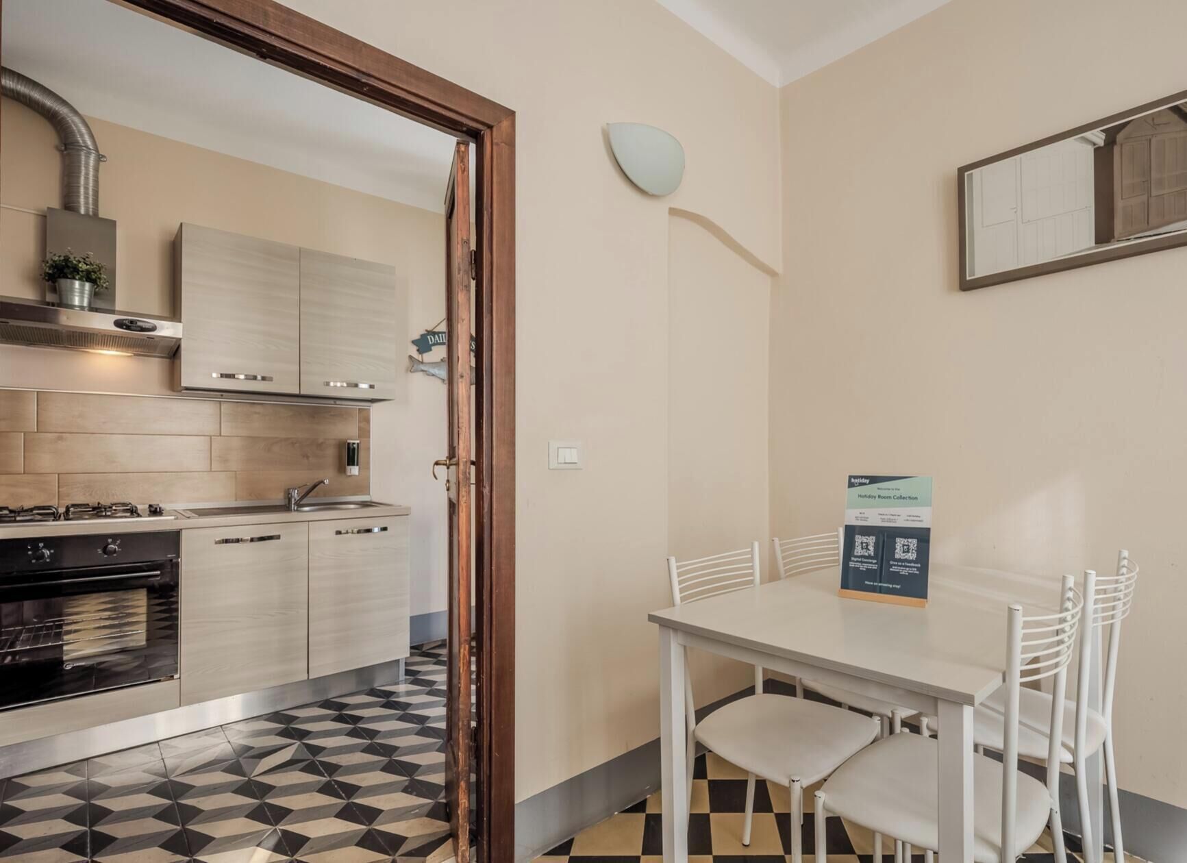 Una cucina compatta con elettrodomestici moderni, una zona pranzo con tavolo e sedie, e uno specchio a parete.