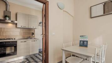 Una cucina compatta con elettrodomestici moderni, una zona pranzo con tavolo e sedie, e uno specchio a parete.