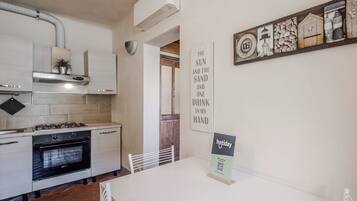 A modern kitchen with white cabinets, a stove, and an oven. There is a dining table with chairs and a sign on it.