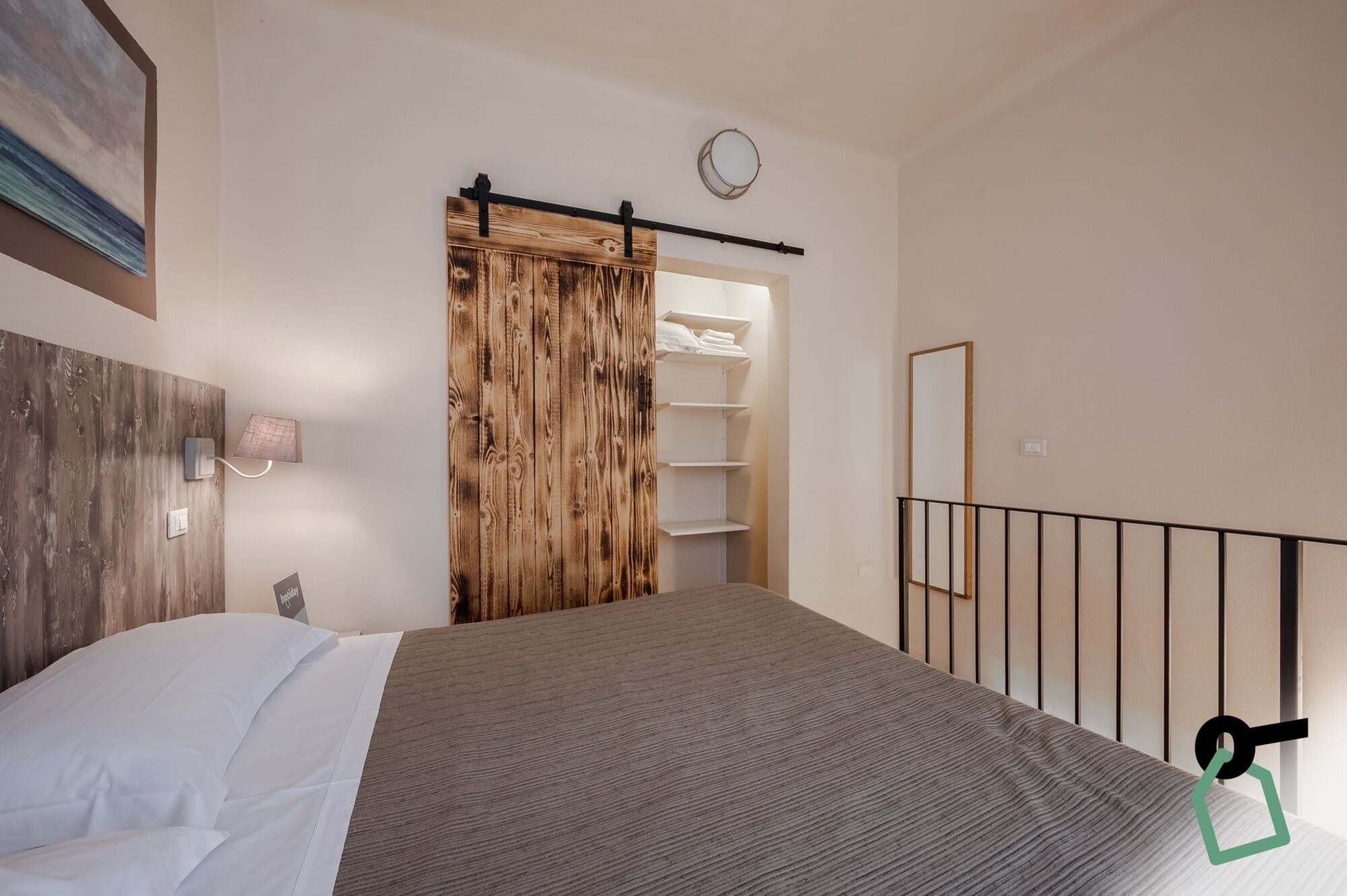 Ein Schlafzimmer mit einem Bett, einem Holzschrank, einem Spiegel und einem Regal mit gefalteter Kleidung.