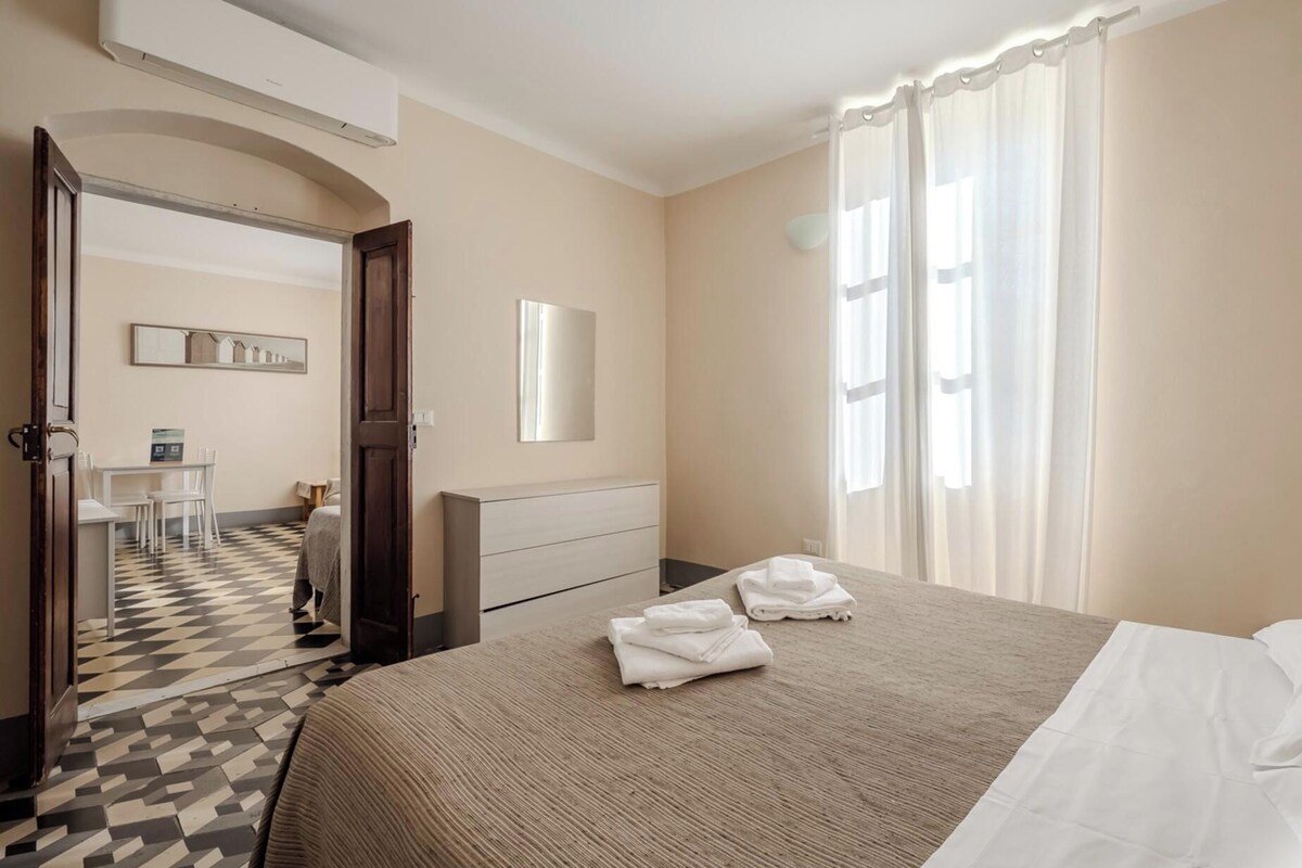 Habitación de hotel con cama, escritorio, silla, espejo y ventana con cortinas.