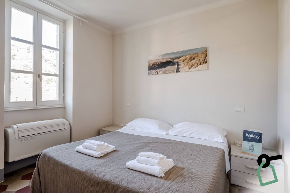 A hotel room with a bed, a radiator, a window, and a painting on the wall.