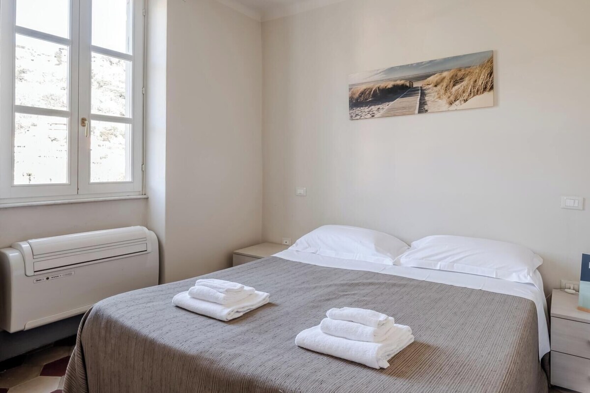 A hotel room with a bed, a window, a radiator, and a painting on the wall.