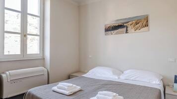 A hotel room with a bed, a window, a radiator, and a painting on the wall.