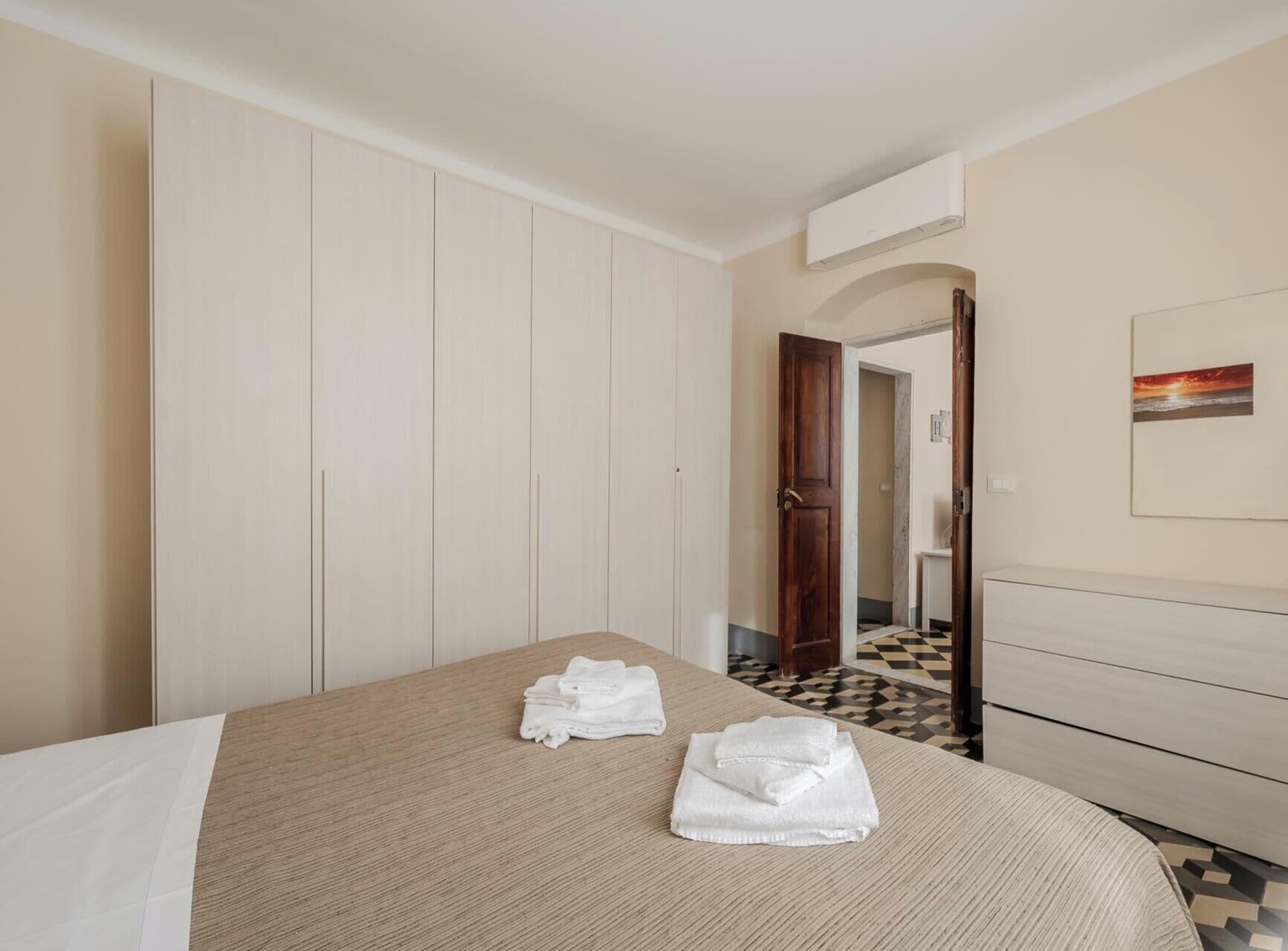A hotel room with a bed, a wooden door, a white wardrobe, and a tiled floor.