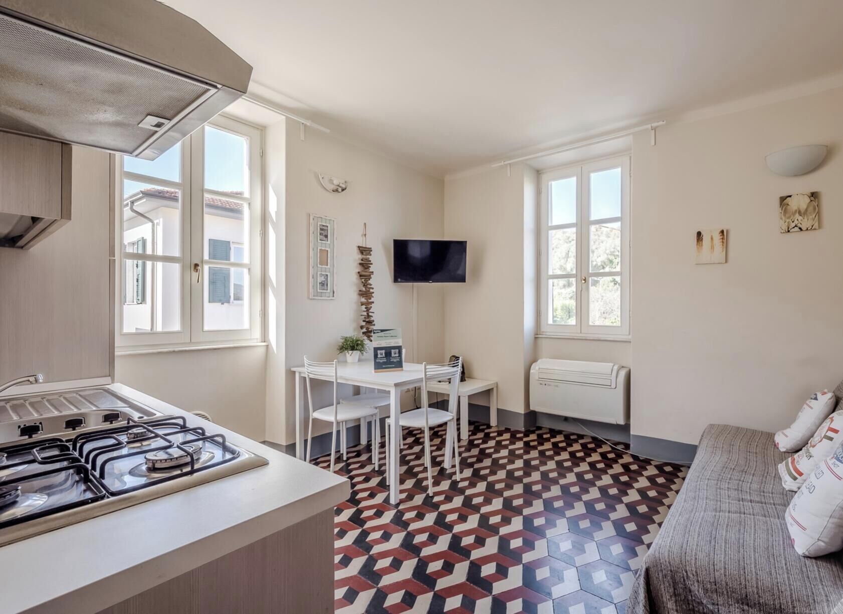 Una cocina compacta con estufa a gas, una mesa de comedor con sillas, un televisor montado en la pared y un suelo estampado.