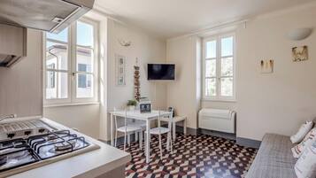 Una cocina compacta con estufa a gas, una mesa de comedor con sillas, un televisor montado en la pared y un suelo estampado.
