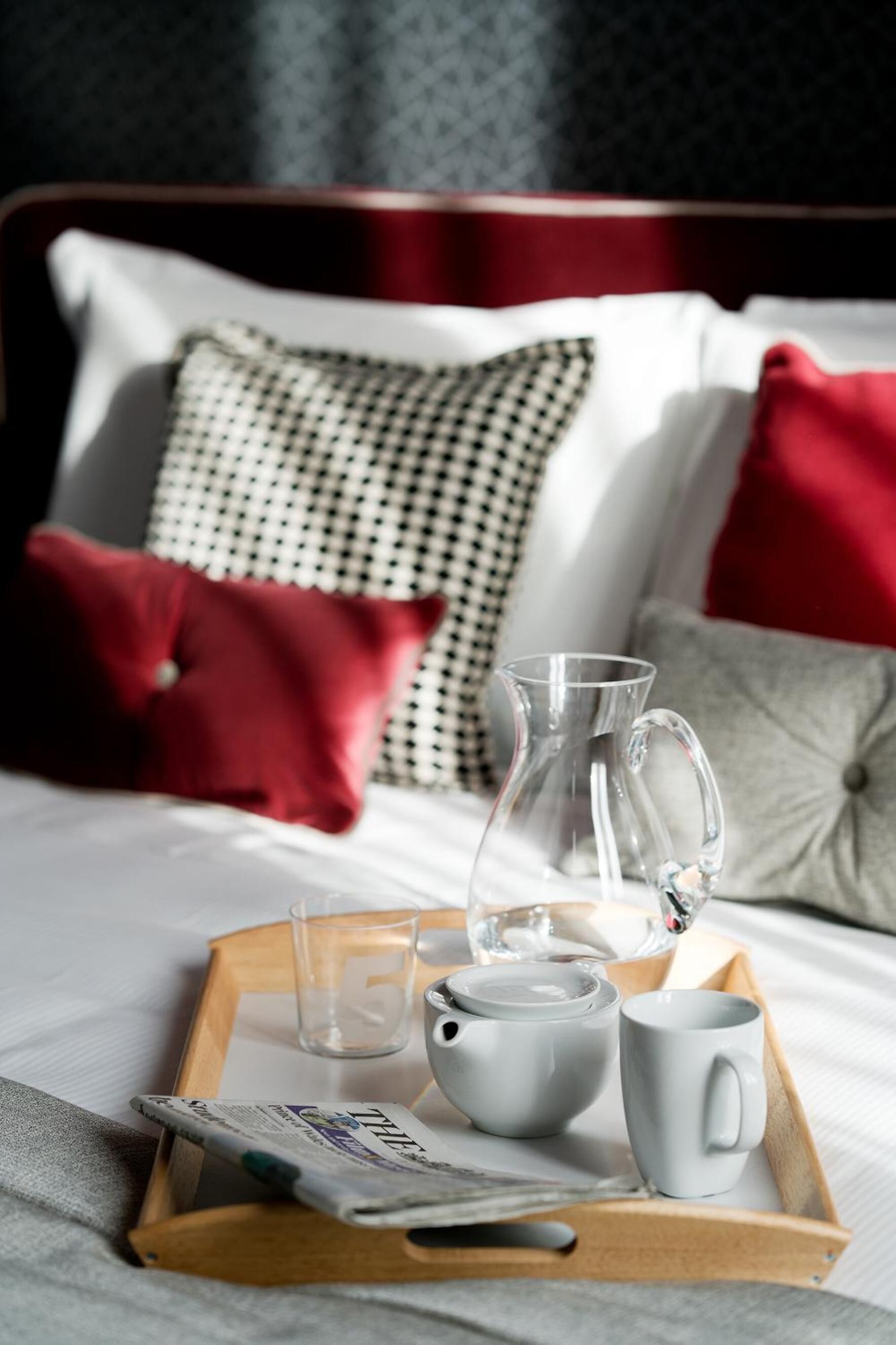 Un letto rifatto con cura e un vassoio per la colazione, con un boccale, una tazza e un giornale.